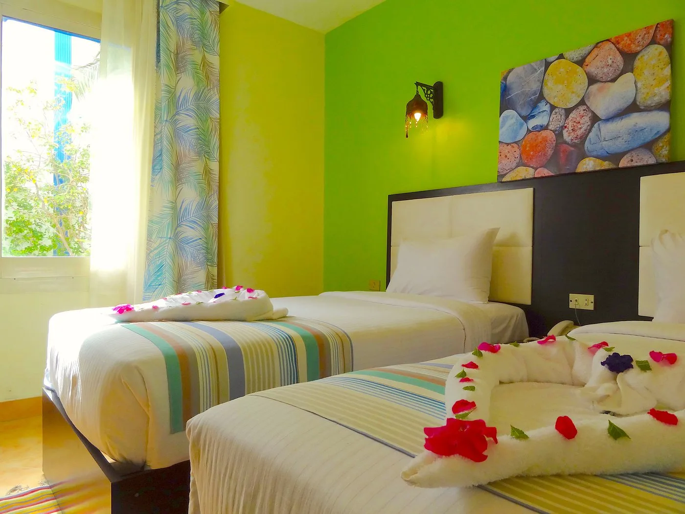Camera con pareti verde e giallo, due letti singoli decorati con fiori e finestra luminosa