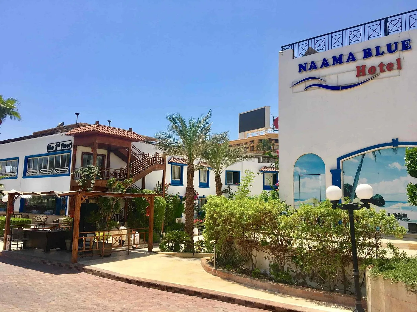 Facciata del Naama Blue Hotel bianco e blu con palme e giardino curato