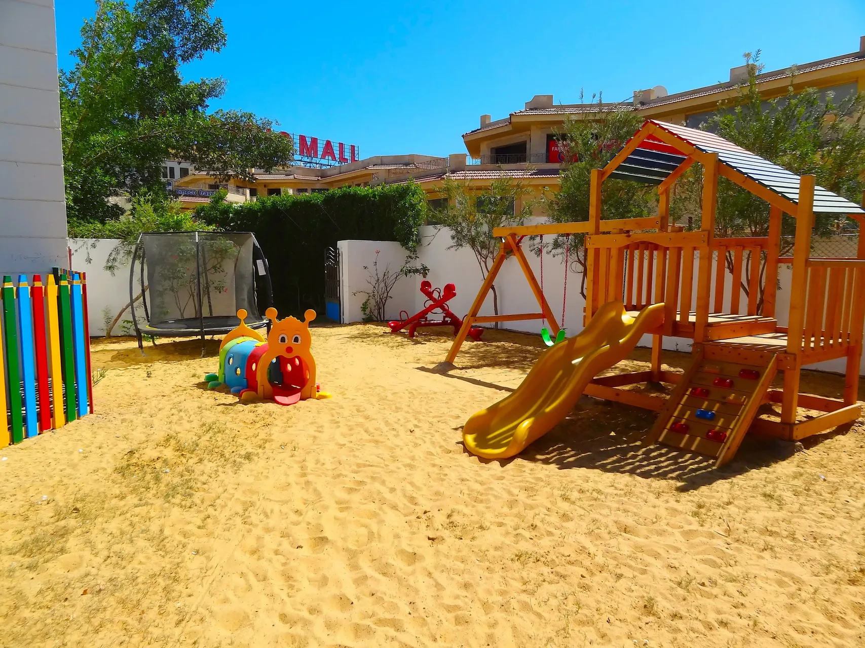 Area giochi per bambini con scivolo in legno, trampolino e giochi colorati su sabbia