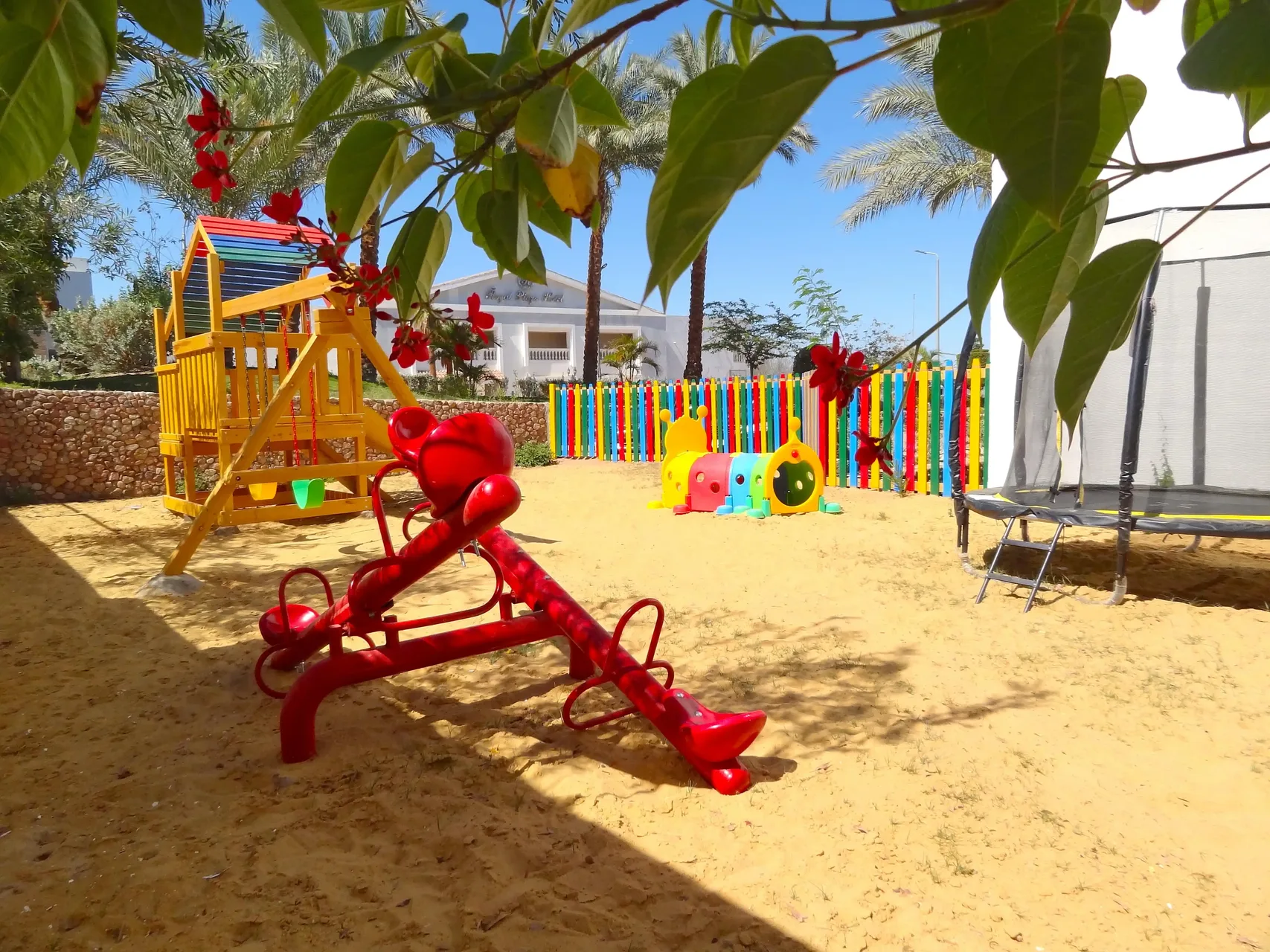 Parco giochi per bambini con altalena a bilico rossa, scivolo e recinzione colorata
