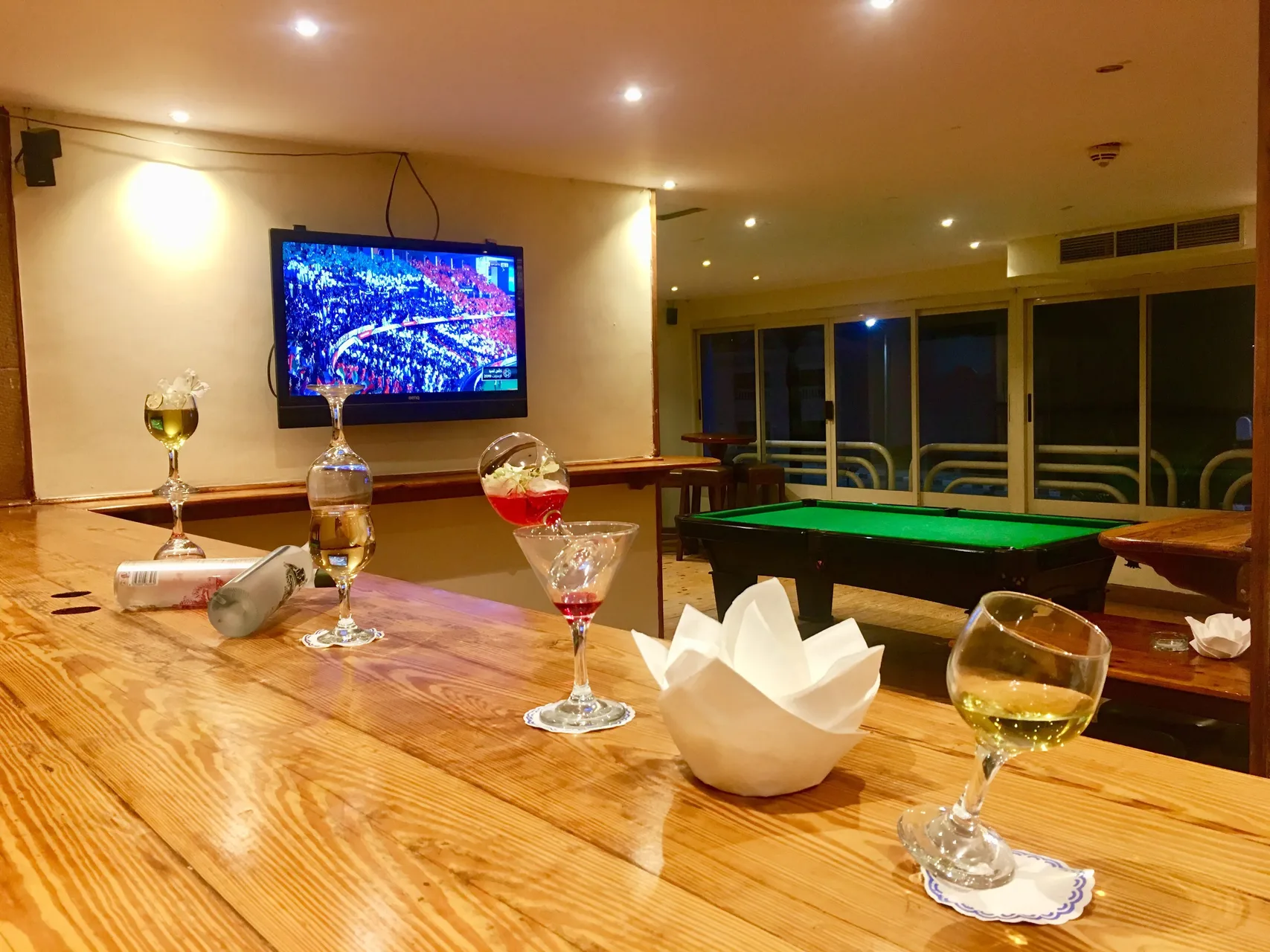 Bancone in legno con cocktail e tavolo da biliardo con TV accesa sullo sfondo