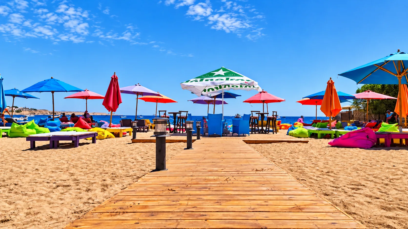 Spiaggia sabbiosa con ombrelloni colorati, pouf e passerella in legno verso il mare