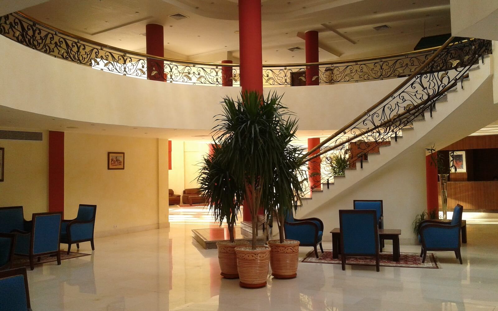 Hall dell'hotel con scala a chiocciola, colonne rosse e poltrone blu