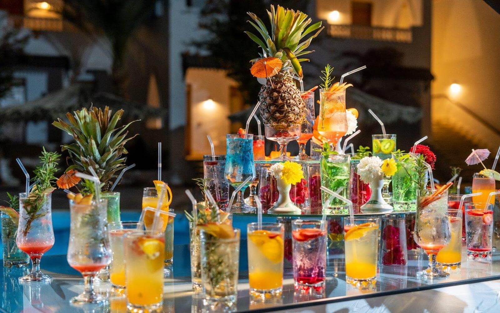 Composizione di cocktail colorati con ananas e fiori su un tavolo a specchio