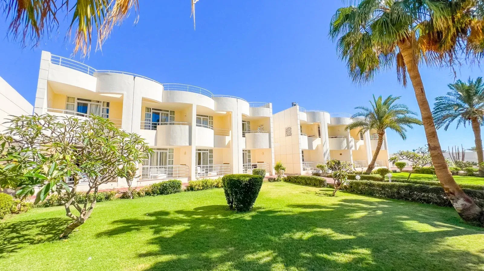 Edifici bianchi del resort con balconi curvi, giardino verde e palme