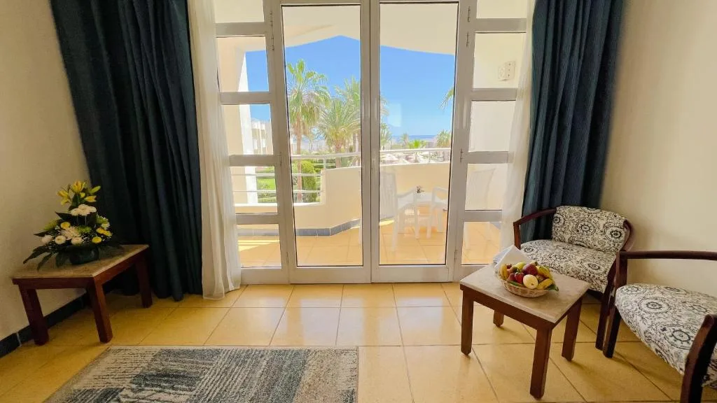 Soggiorno della camera con poltrone, tavolino con frutta e porta finestra sul balcone