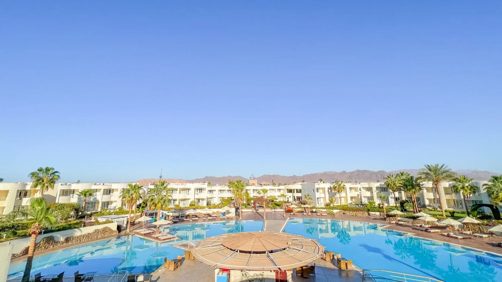 Vista panoramica del resort con ampie piscine, palme e montagne sullo sfondo