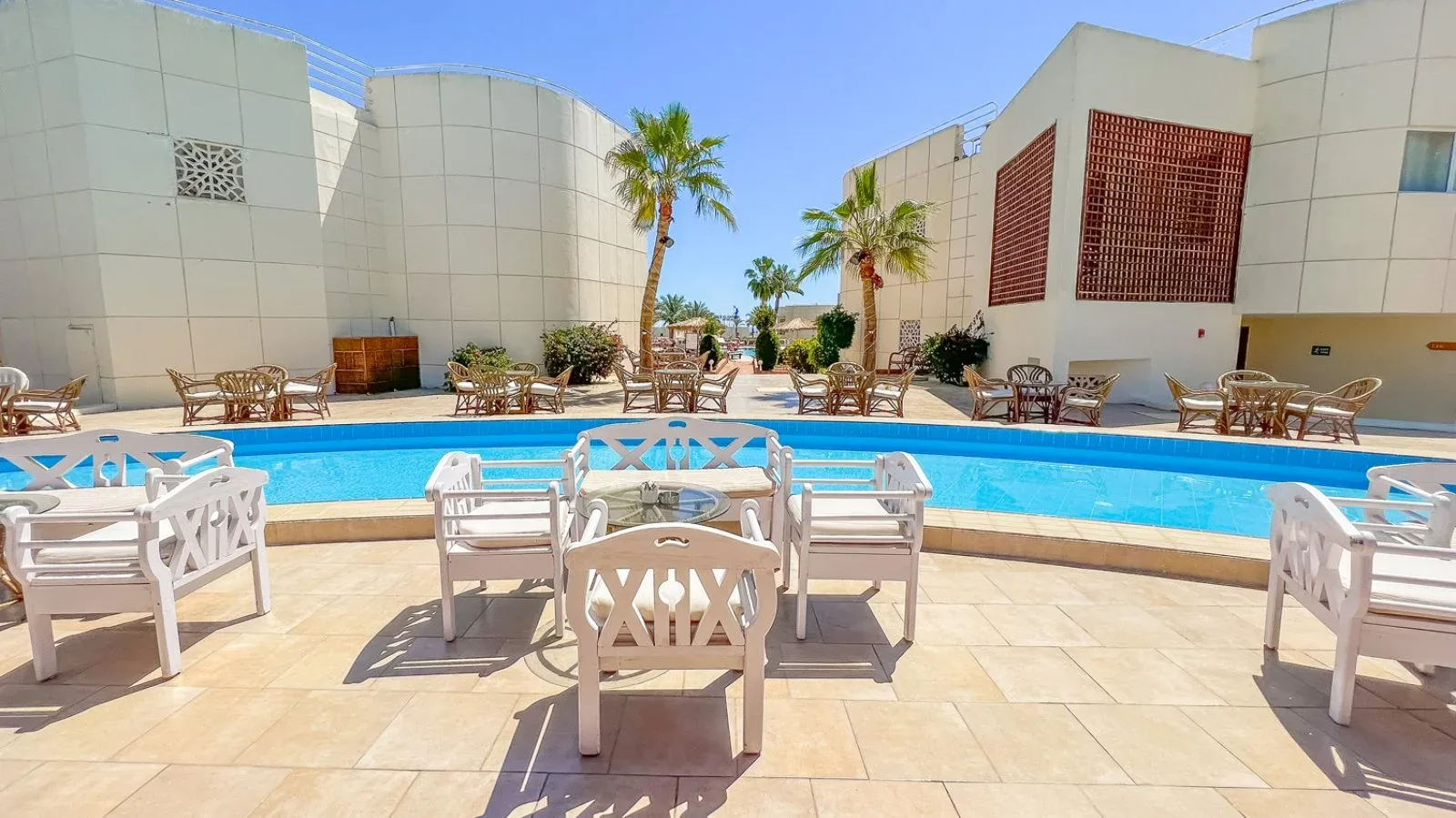 Piscina circondata da poltrone bianche e tavolini tra edifici bianchi del resort