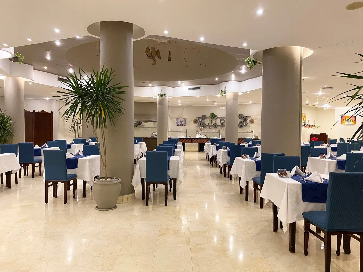 Ristorante interno luminoso con tavoli apparecchiati, sedie blu e colonne