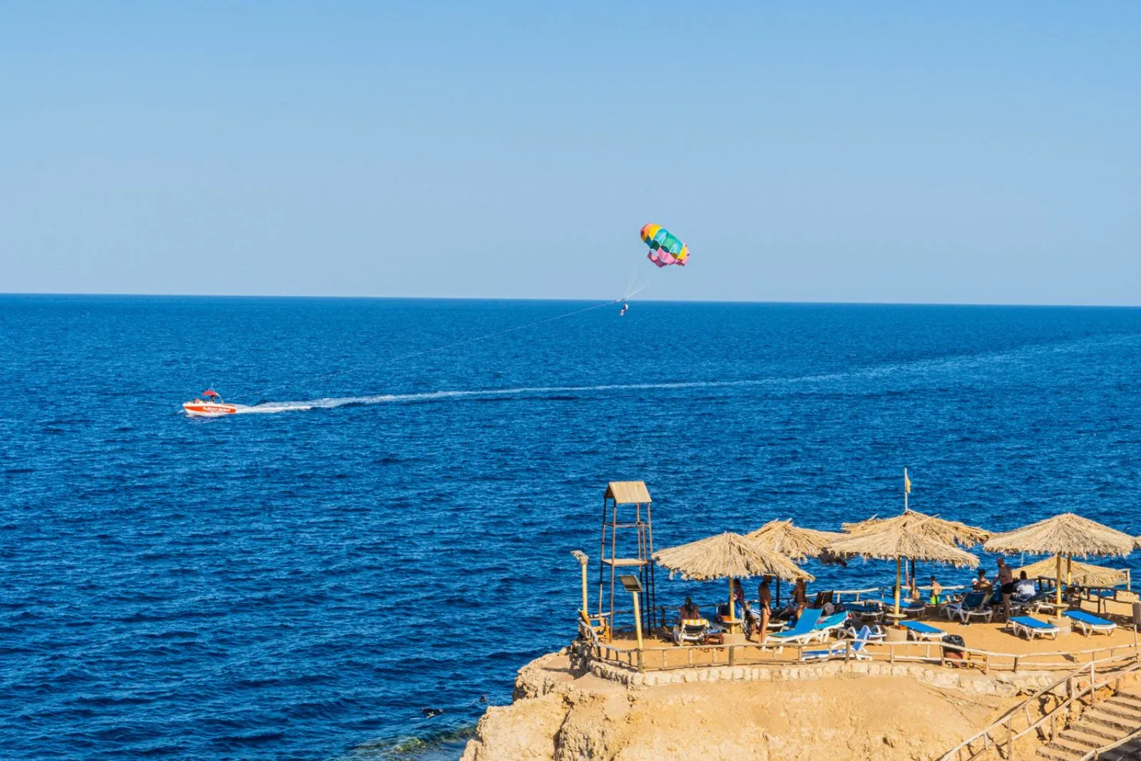 Parasailing colorato sul mare blu con spiaggia su scogliera e ombrelloni di paglia