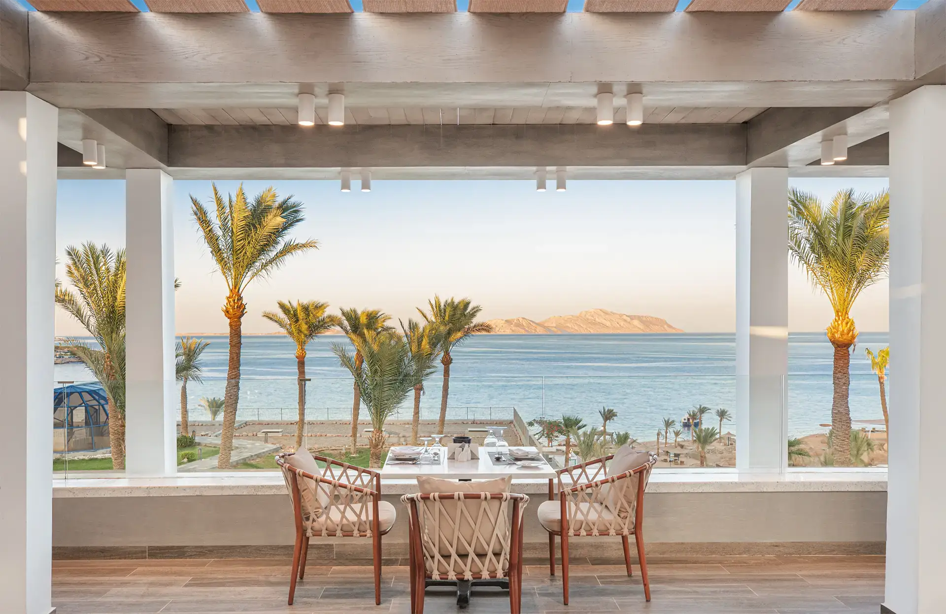 Tavolo apparecchiato sotto pergolato con vista panoramica sul mare e palme